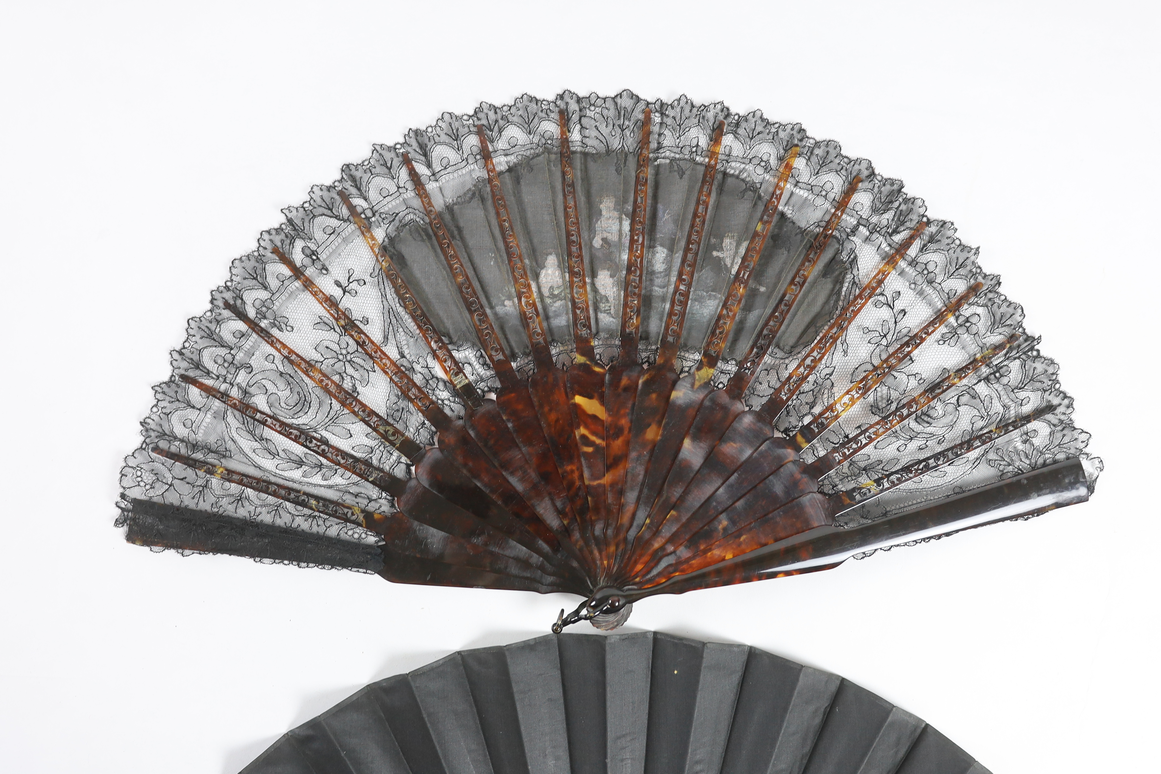 A late Victorian Chantilly black lace and tortoiseshell fan with a central painted cartouche and a mother of pearl and hand painted fairy and cherub fan, indistinctly signed